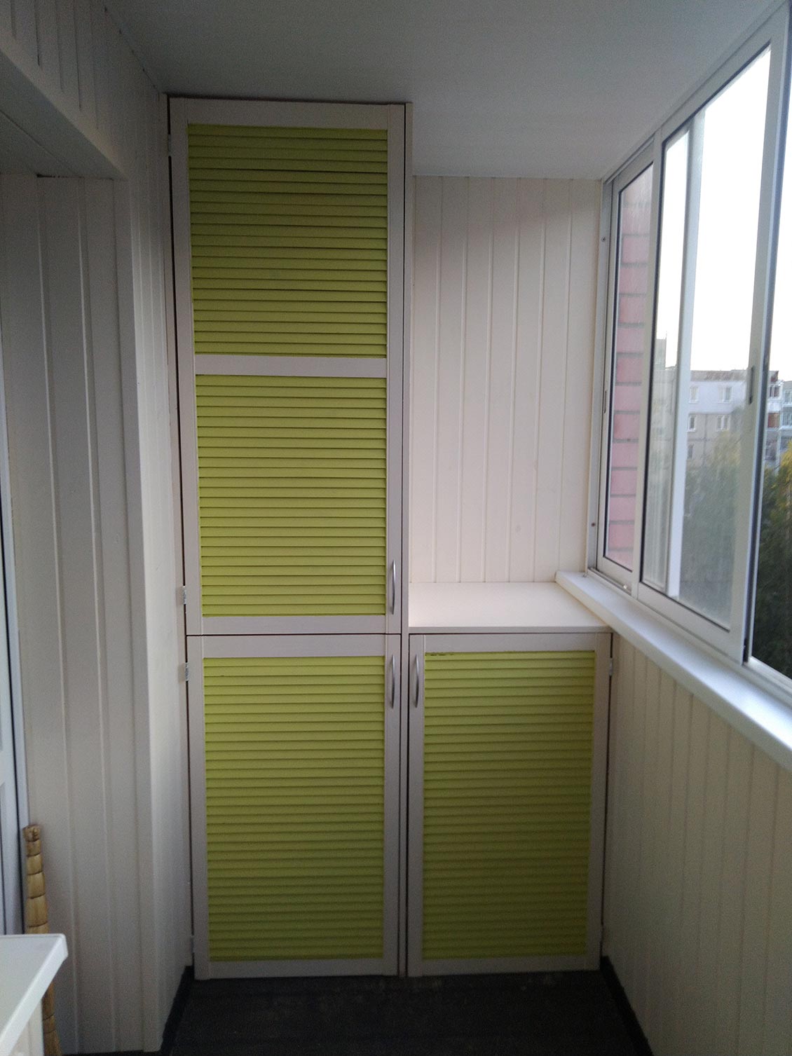Бело-зеленный деревянный шкаф на балконе с жалюзийными дверями